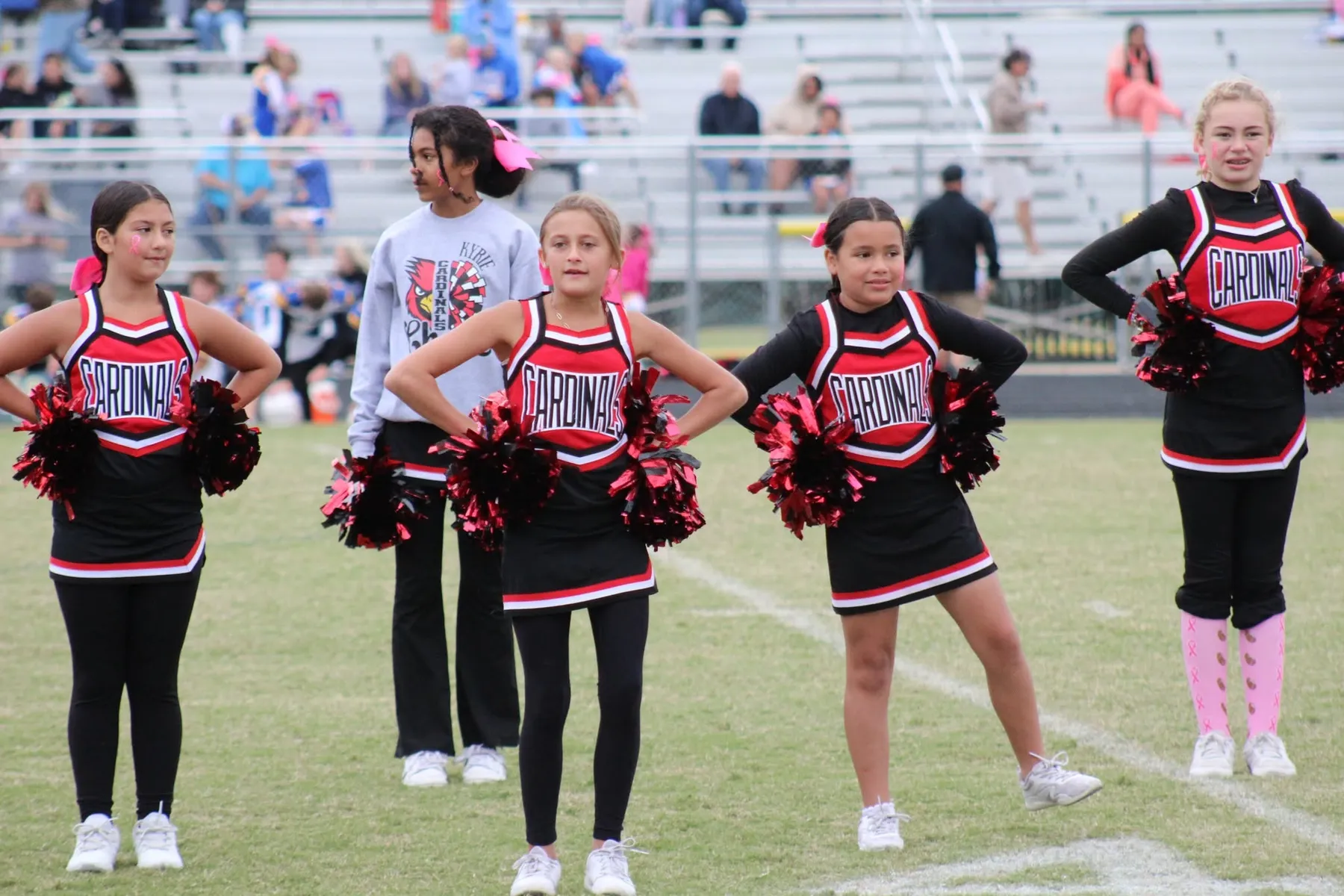 Four Oaks Cardinals cheerleaders with red and black pom-poms on the field