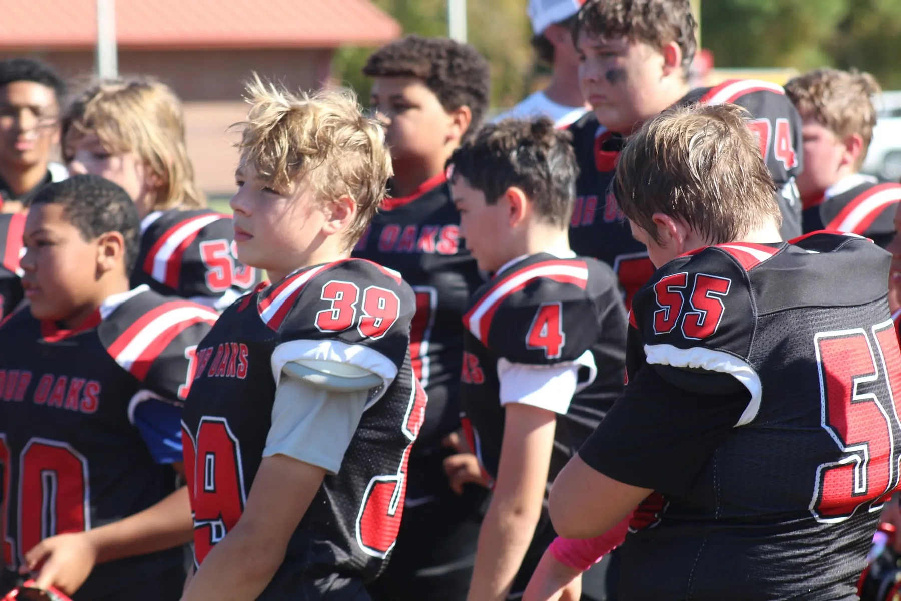 Four Oaks teammates in black jerseys standing close together on the sideline
